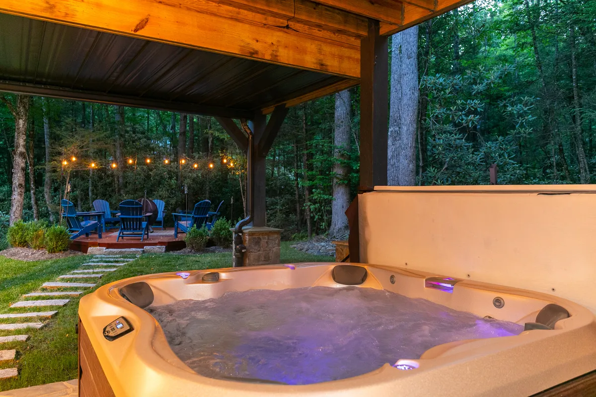 This exterior image highlights an inviting hot tub surrounded by string lights and a comfortable outdoor seating area. Set against lush greenery, the scene evokes a sense of intimacy and tranquility, perfect for private relaxation or small gatherings under the stars.