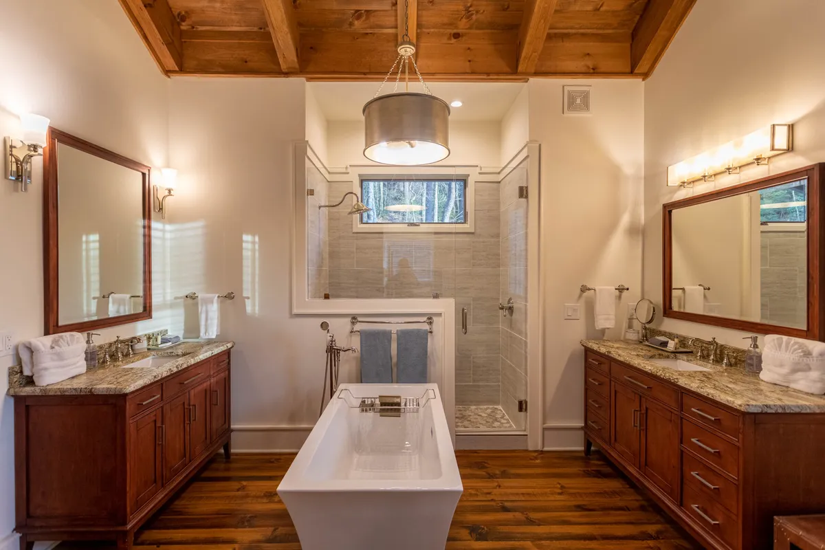 A spa-inspired bathroom with a freestanding soaking bathtub, double granite vanity sinks, large mirrors, and rustic wooden ceiling beams. The scene is elegant and tranquil, evoking a high-end spa experience.