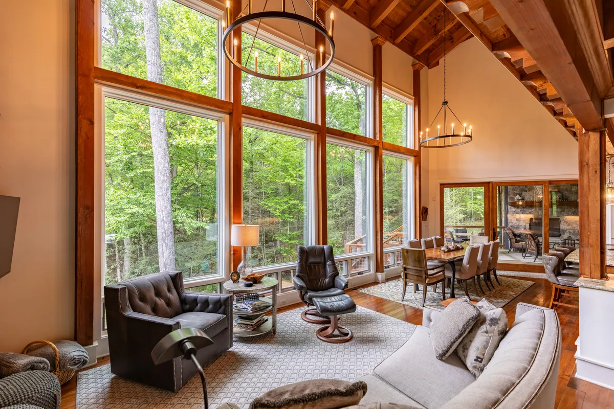 A bright and spacious living and dining area with large windows framing mountain views, exposed wooden beams, stylish seating, and an inviting dining table. The room is filled with natural light and offers a welcoming spot for reading, dining, and watching the seasons change.