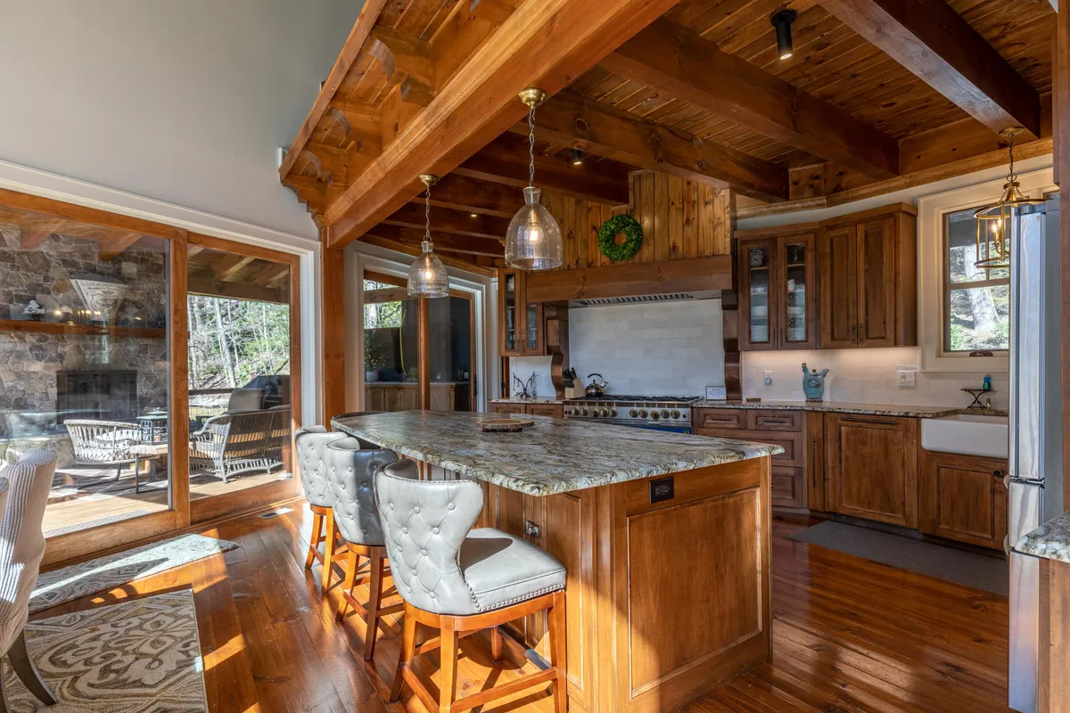 A beautifully appointed kitchen area featuring an expansive island countertop, rich wooden cabinetry, glass pendant lights, and large windows that bathe the space in natural light. The kitchen is set up for cooking, entertaining, and family gatherings.