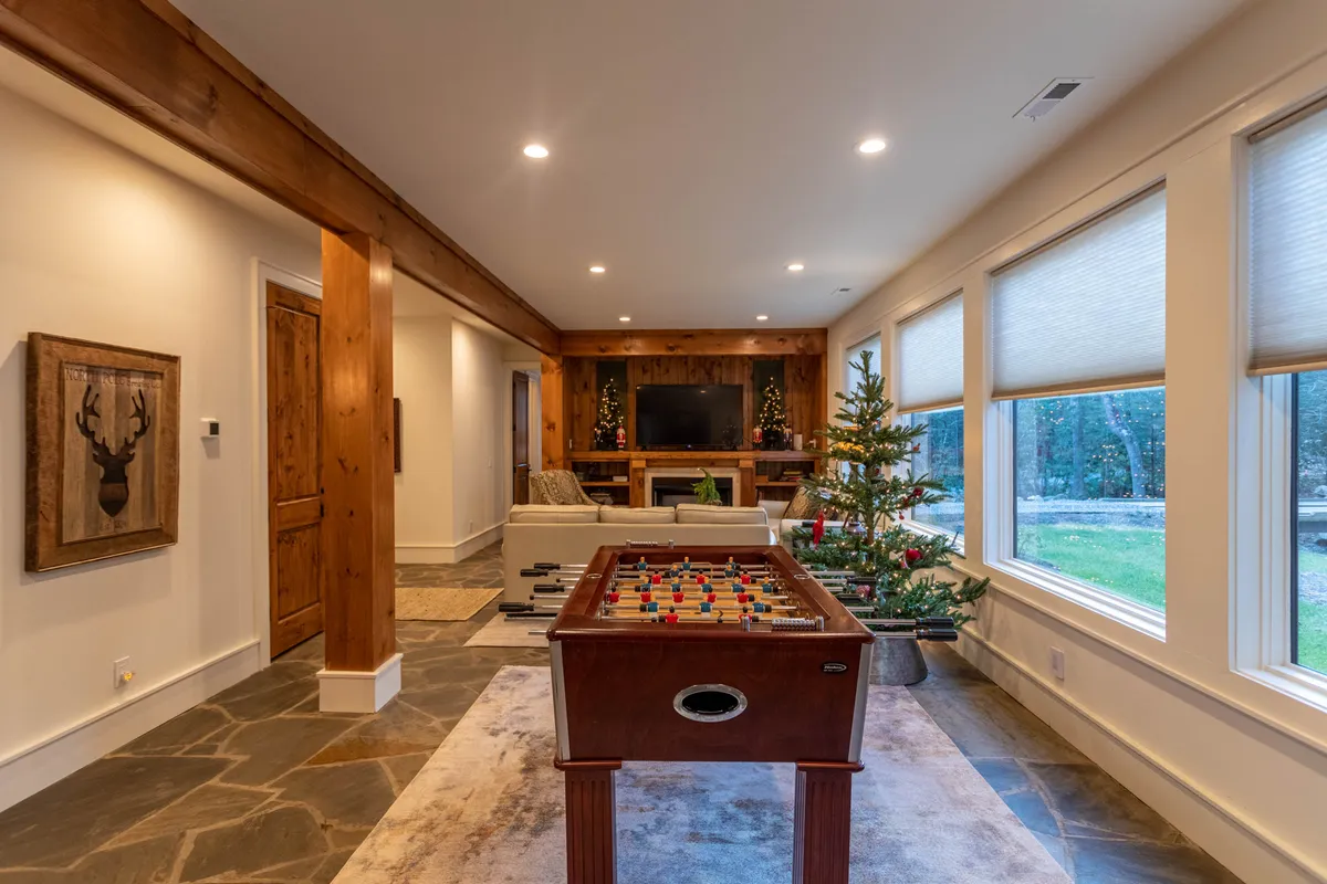 A playful entertainment den with a foosball table, comfortable sofa, TV console, and a festive touch from the Christmas tree. The space is suited for both kids and adults to hang out, play games, or enjoy cozy evenings.