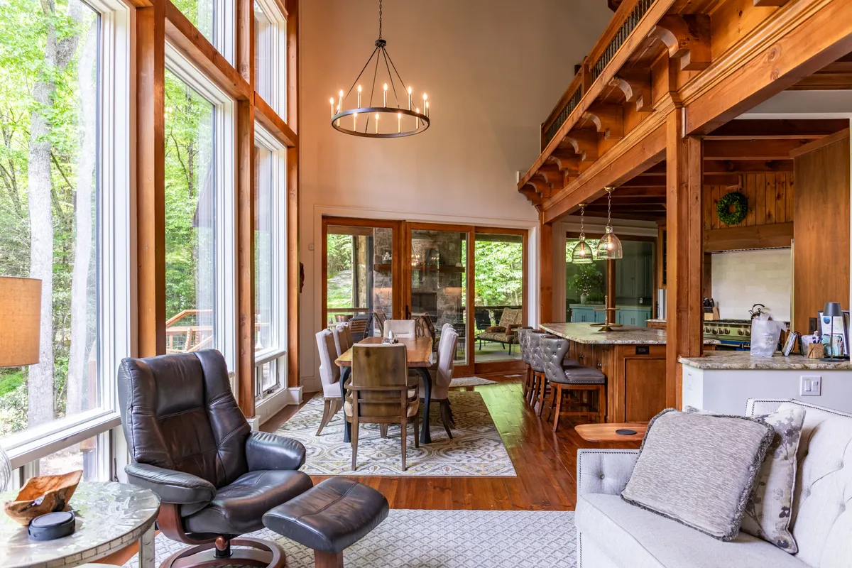 A bright, open-plan dining and kitchen area featuring a spacious dining table, an island with seating, and a view into the adjoining living space. The windows bring in sunlight and offer glimpses of the outdoors, while the kitchen showcases high-end appliances and granite counters.