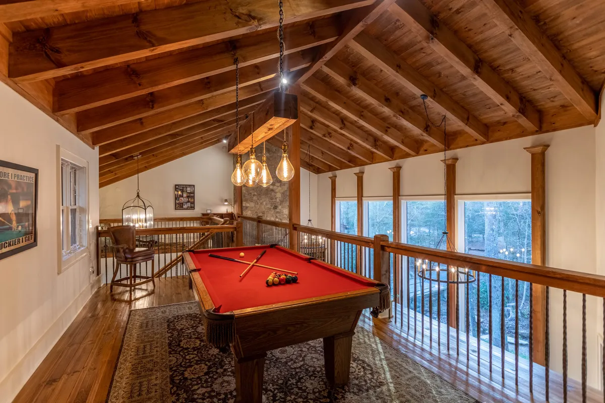 A cozy interior game room with a pool table, exposed wooden beams, large windows letting in natural light, and stylish hanging lights. The inviting setup is ideal for both kids and adults to play games, socialize, and unwind after spending time outdoors.